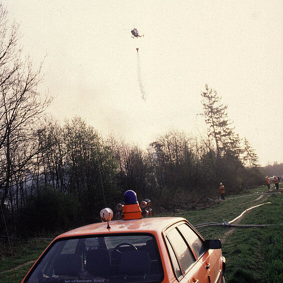 Der Einsatzleitwagen (ELW) des Kommandanten der FF München und ein Hubschrauber der Polizei mit einem Außenlastbehälter im Einsatz im Forstenrieder Wald